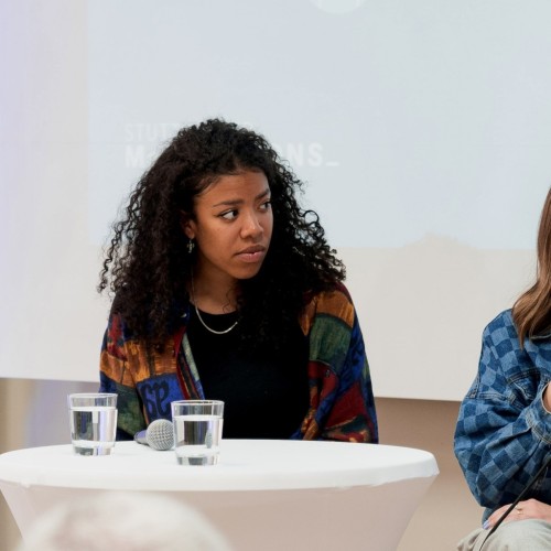 Lia Gavi sitzt zuhörend bei einer Podiumsdiskussion